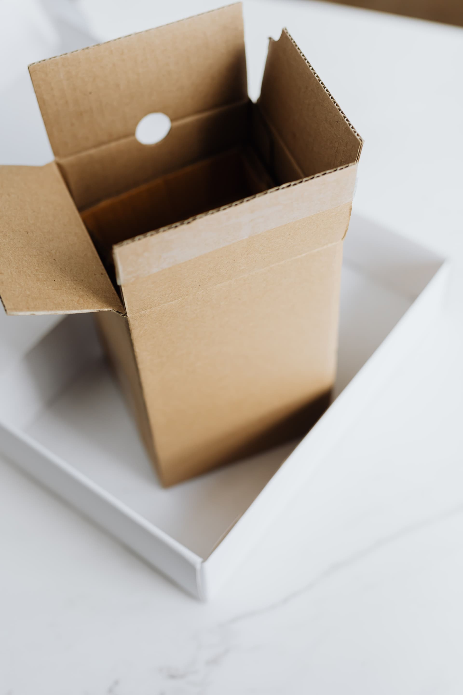 An open brown cardboard box sitting inside a larger white box on a pale marble surface, both empty.